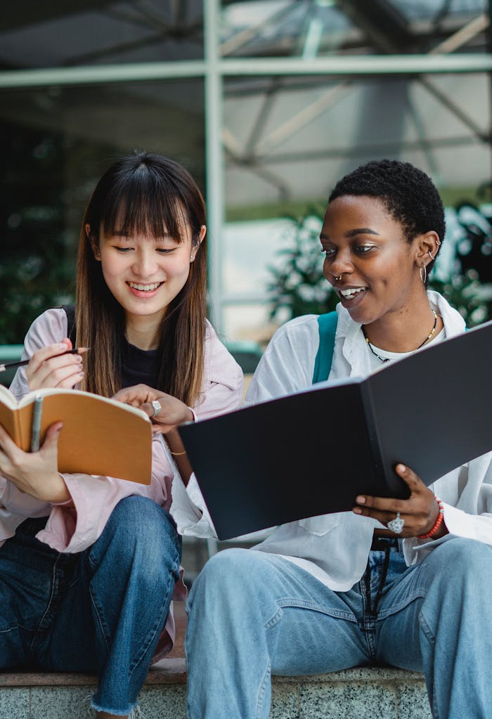 Happy young multiracial women in casual clothes preparing for exam with notebook outside in summer day