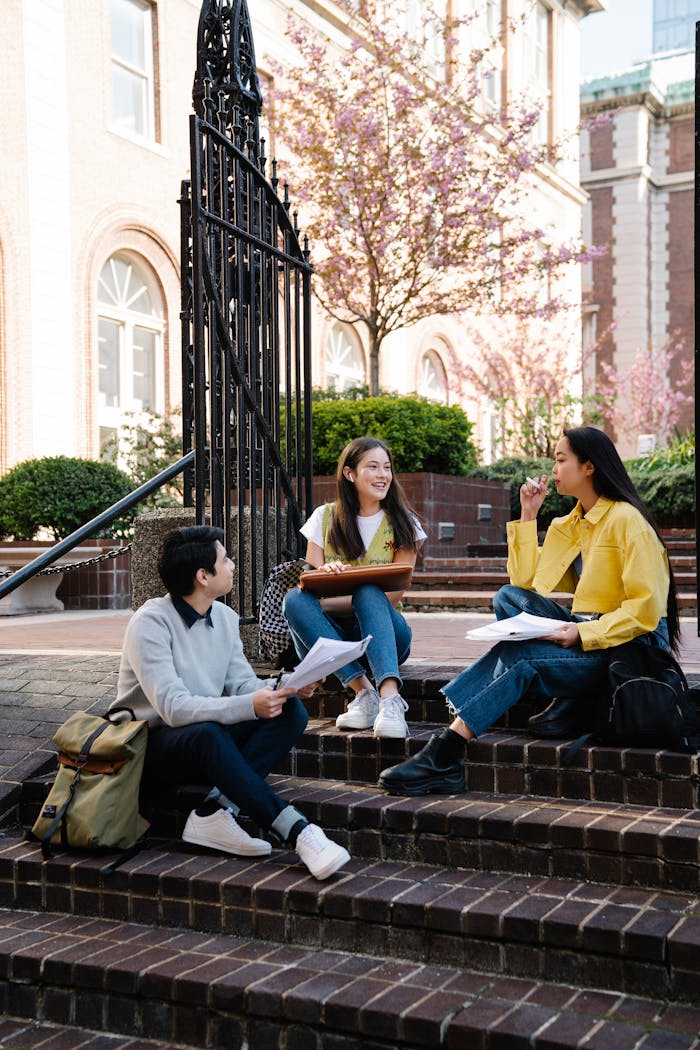 Three students sitting on steps, enjoying outdoor study session on a sunny day.